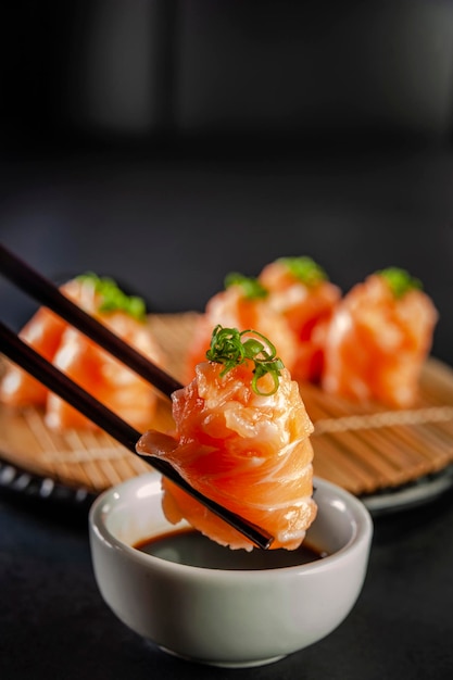 Salmon Jhow sushi on chopsticks on a container with soy sauce. Closeup.