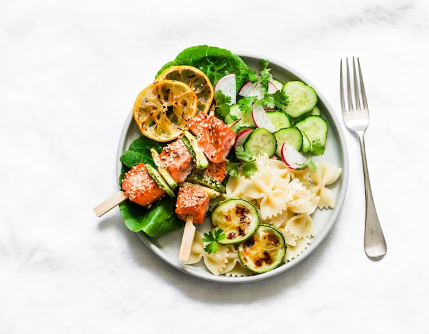 Salmon roasted skewers with zucchini pasta and vegetables salad on a light background top view Delicious healthy balanced lunch