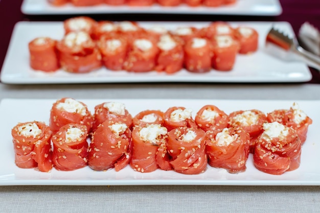 Salmon rolls stuffed with cheese sprinkled sesame seeds laid on a transparent glass plate