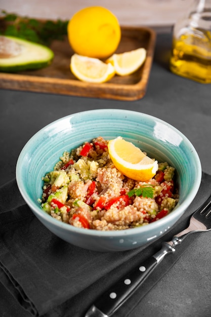 Salmon salad with tomatoes, avocado and quinoa in a blue bowl on a dark gray table vertical photo, a dish of balanced diet.