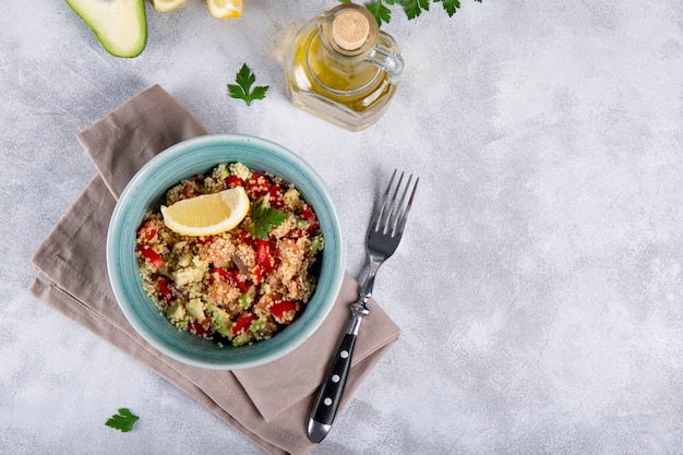 Salmon salad with tomatoes avocado and quinoa in a blue bowl on a light gray table top view a dish