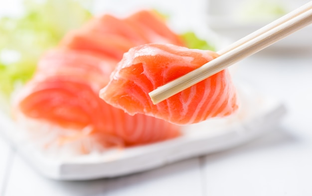 salmon sashimi set with chopsticks holding a piece of sliced salmon