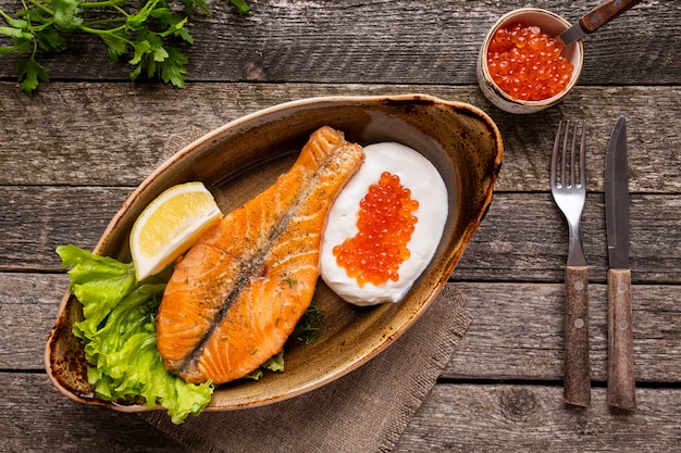 Salmon steak  cream and red caviar served  fork and knife. Top view