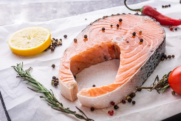 Salmon steak, red fish lies on parchment paper, next to lemon pepper tomato and herbs