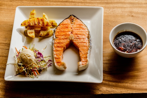 Salmon steak in a white plate on a wooden table.