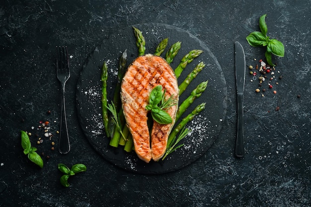 Photo salmon steak with baked asparagus and spices on a black stone plate top view free space for your text