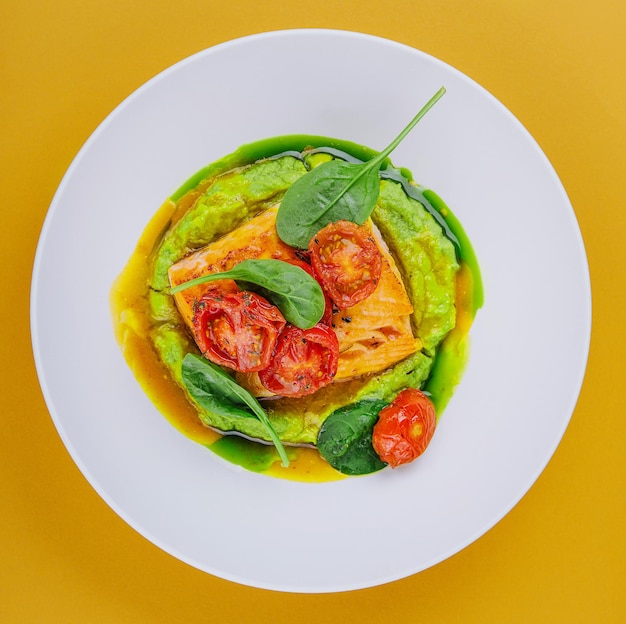 Salmon steak with mashed avocado decorated with basil leaves and cherry tomatoes