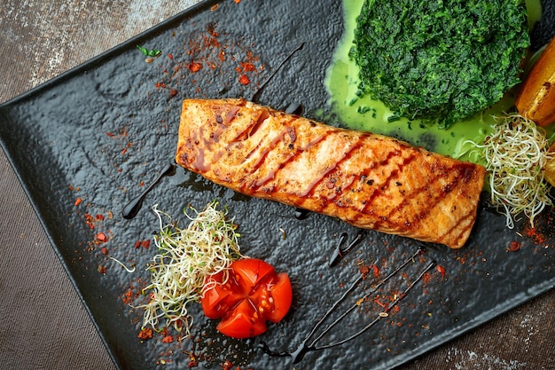 Salmon steak with stewed spinach in cream on a black plate