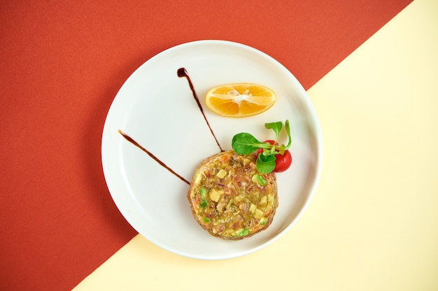 Salmon tartare with avocado and lemon in a white plate on colored surface.