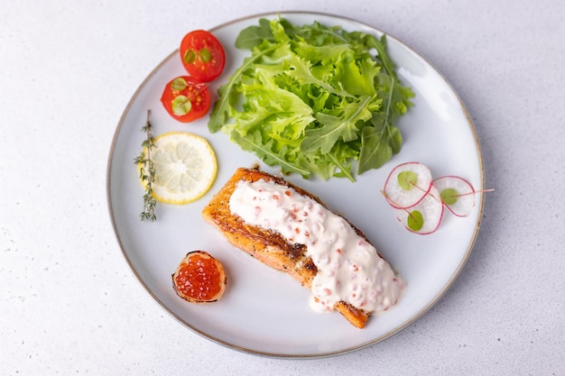 Salmon trout with creamy Champagne sauce with red caviar arugula cherry tomatoes radish and lemon Traditional French dish Selective focus closeup top view