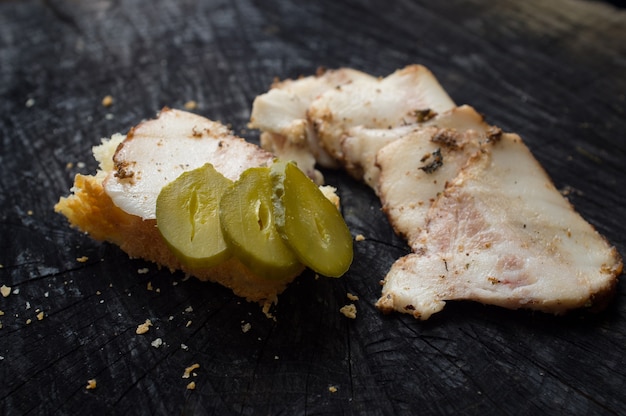 Salo appetizer with pickled cucumber slices on wooden black desk