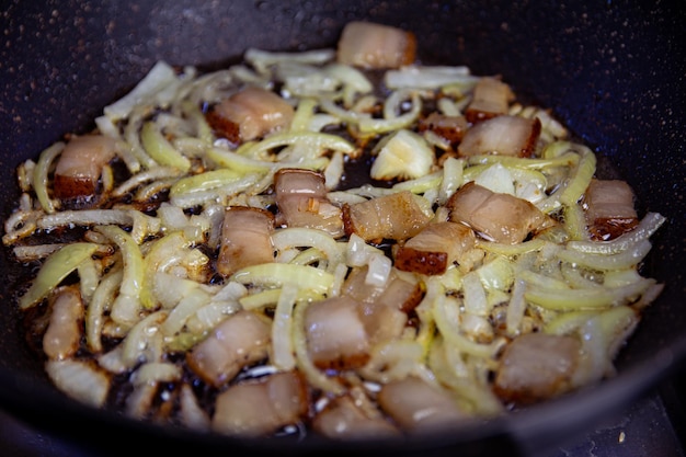 Salo and finely chopped onion are fried in a black frying pan