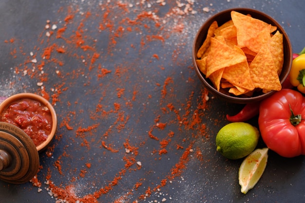 Photo salsa tomato sauce and nacho chips on dark background with flecks of salt and powdered red pepper or paprika food and culinary condiments spices mix on rough textured surface free space concept