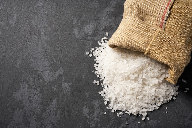 Salt are poured out of the bag on black stone background, top view.