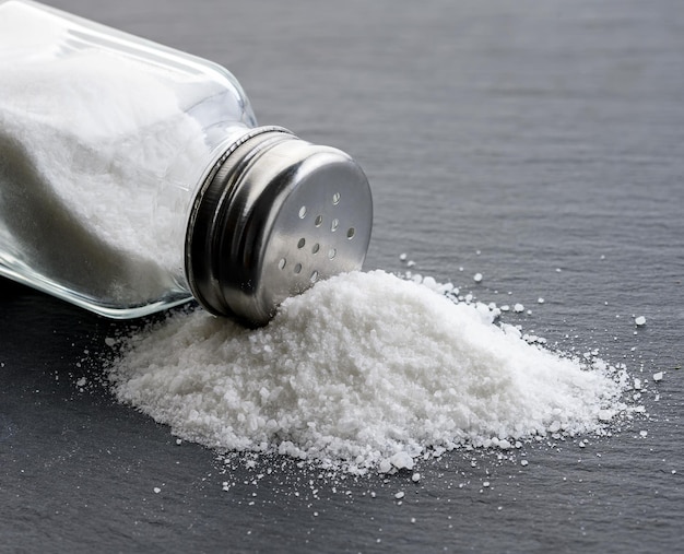 Salt glass jar and pile of spilled salt on a slate stone plate