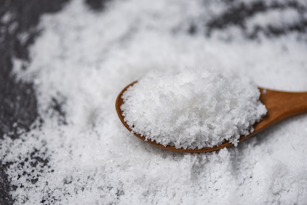 Salt in wooden spoon and heap of white salt on dark 