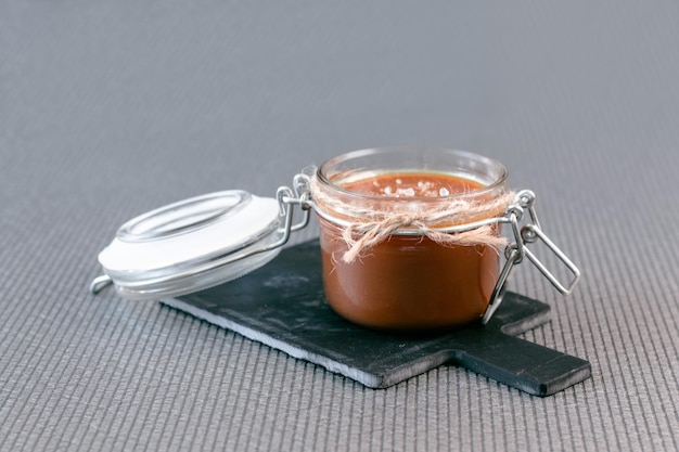 Salted caramel in a jar on a gray background on a stone stand. Side view.