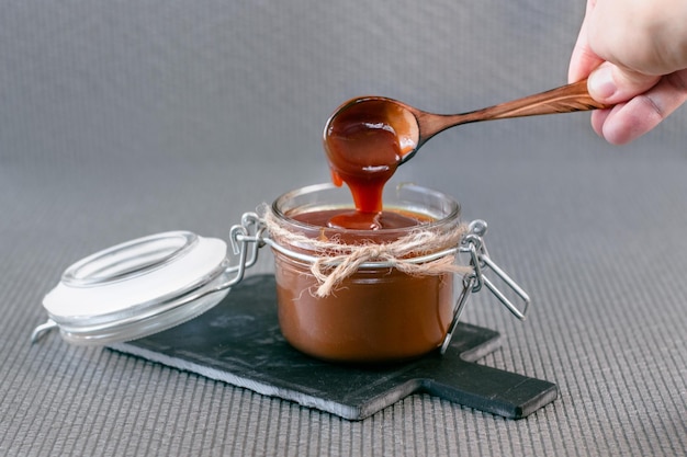 Salted caramel in a jar on a gray background on a stone stand. Side view.