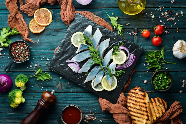 Salted herring with onion and lemon on a black stone board Top view Free space for your text