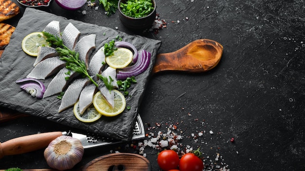 Salted herring with onion and lemon on a black stone board Top view Free space for your text