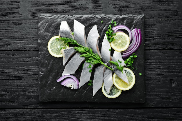 Salted herring with onion and lemon on a black stone board Top view Free space for your text