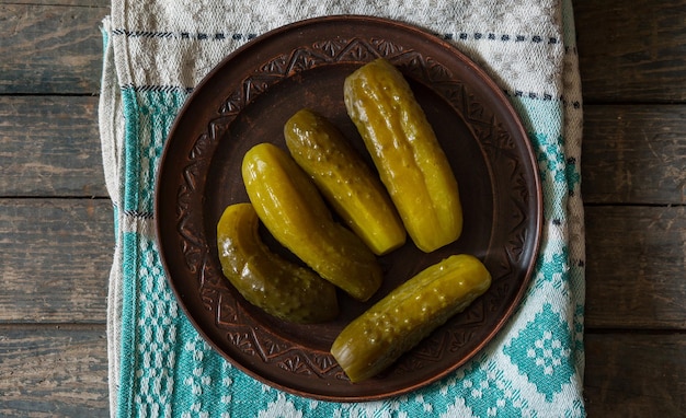 Salted pickled cucumbers in a brown plate on a towel on a wooden texture