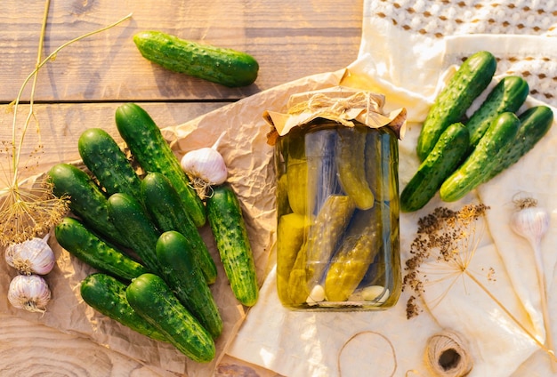 Salted pickled cucumbers in a jar on a wooden table in the garden Cucumbers herbs dill garlic Preservation conservation Background copy spaceTop view