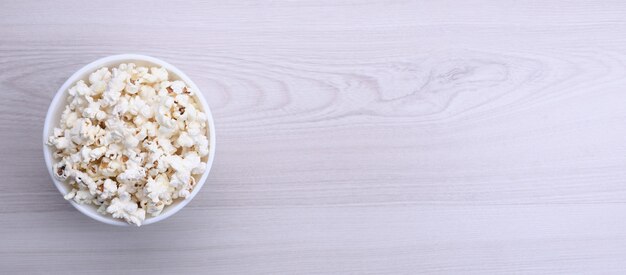 Salted popcorn in a bowl on a wooden table. Top view.