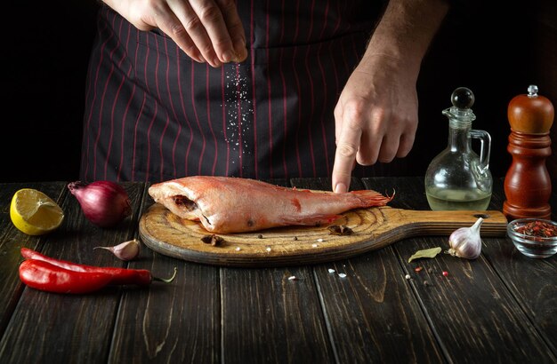 Salting fresh Sebastes fish in the kitchen before baking The cook sprinkles salt on the fish