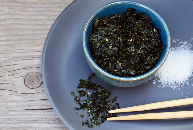 Salty roasted dried seaweed nori with sesame seeds in a blue bowl on old wooden table