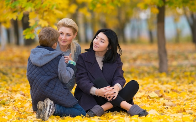 A same sex female couple listening to their son intently in an autumn park setting.