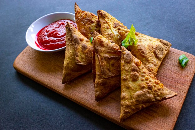 Samosa samsa or somsa are triangular fried pastries or pastri served with tomato sauce and leek slice on black background