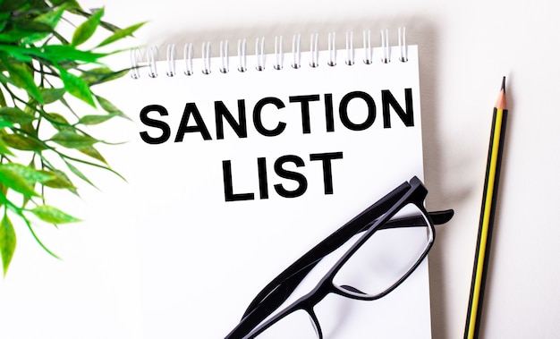 SANCTION LIST written in a white notebook next to a pencil