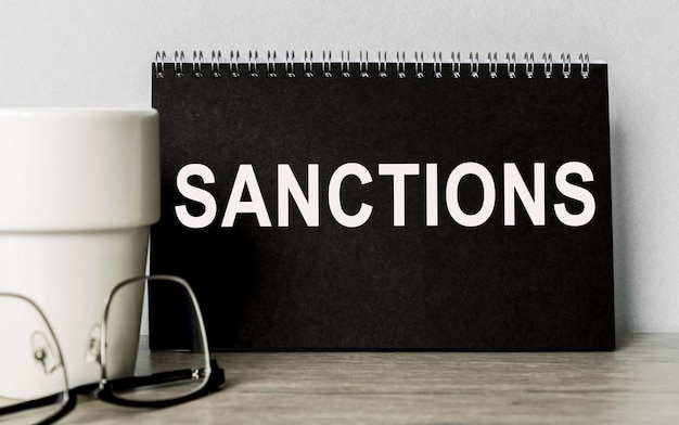 Sanctions Note on a black notepadGlasses a mug on the table