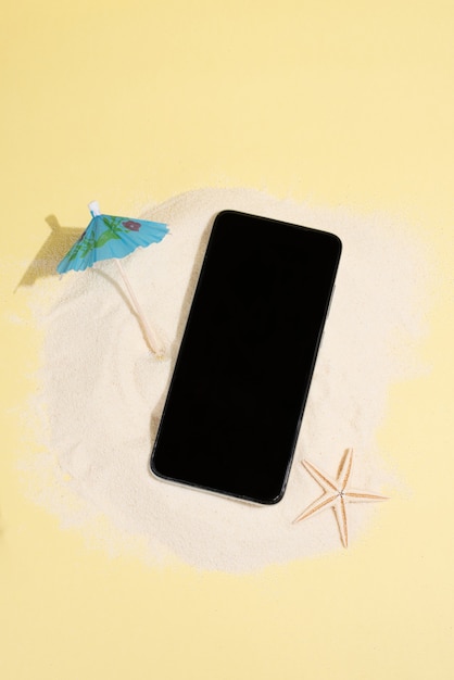 Sand island with smartphone, umbrella and starfish on yellow background, summer concept, mock-up, close up.