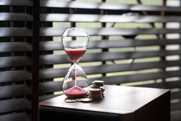 Sand running or flowing down of an hourglass with coins next to it