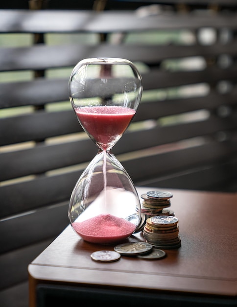 Sand running or flowing down of an hourglass with coins next to it