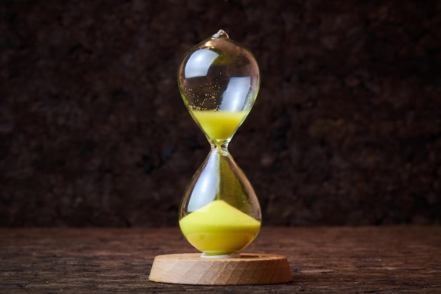 Sand running through the bulbs of an hourglass on a dark cork tree background