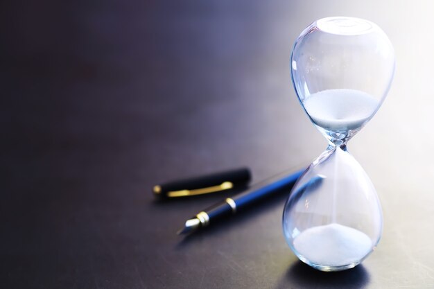 Sand running through the bulbs of an hourglass measuring the passing time in a countdown to a deadline, on a dark table background with copy space.