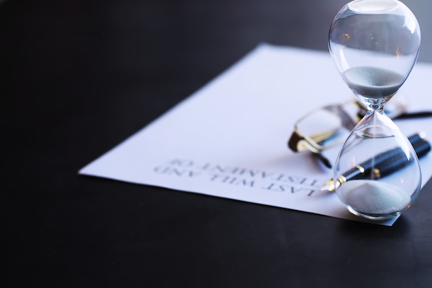 Sand running through the bulbs of an hourglass measuring the passing time in a countdown to a deadline, on a dark table background with copy space.