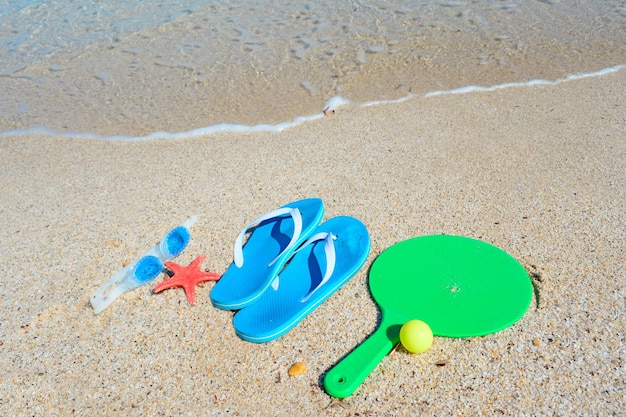 Sandals rackets and sea goggles on a golden shore