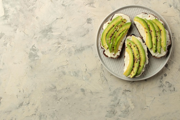 A sandwich of bread and slices of avocado on a plate on a light concrete background making sandwiches top view