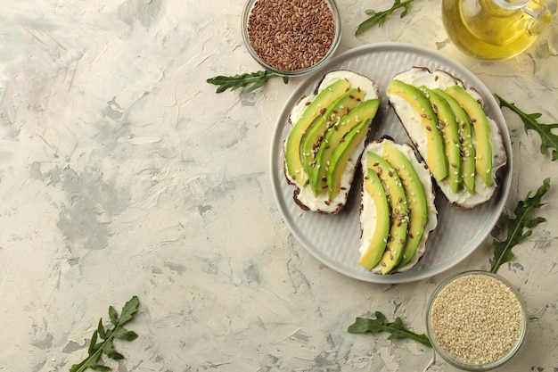 A sandwich of cream cheese bread and slices of avocado on a plate on a light concrete background making sandwiches top view