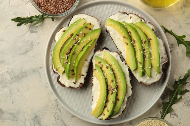 A sandwich of cream cheese bread and slices of avocado on a plate on a light concrete background making sandwiches top view