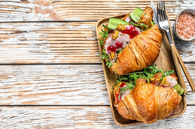 Photo sandwich croissant with ham and cheese on wooden board. white wooden background. top view.