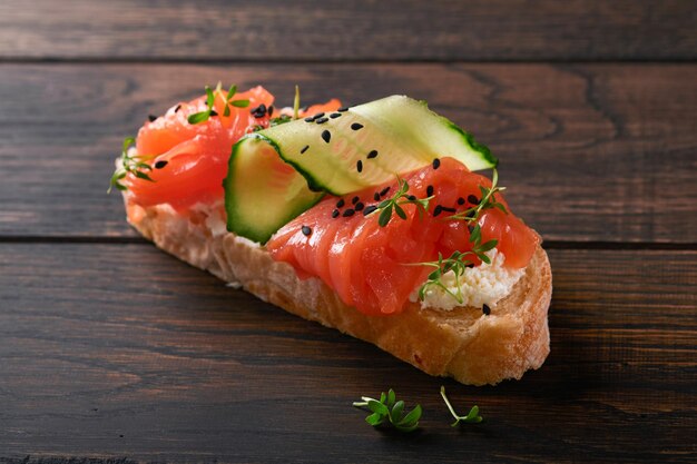 Sandwich Salmon toast with cream cheese cucumber black sesame and microgreens on old wooden table background Seafood Healthy food Photography in low key Top view