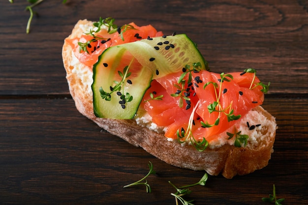 Sandwich Salmon toast with cream cheese cucumber black sesame and microgreens on old wooden table background Seafood Healthy food Photography in low key Top view