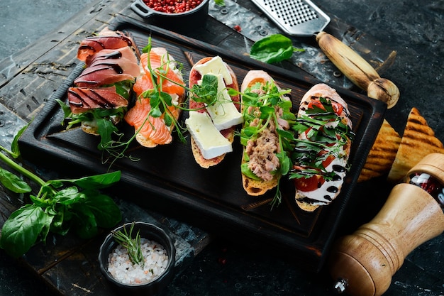 Sandwich Set bruschetta with tuna cheese prosciutto and tomatoes on a dark wooden board On a black stone background