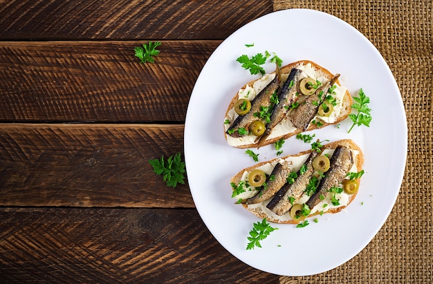 Sandwich - smorrebrod with sprats, green olives and butter on wooden table. Danish cuisine. Top view, overhead, flat lay