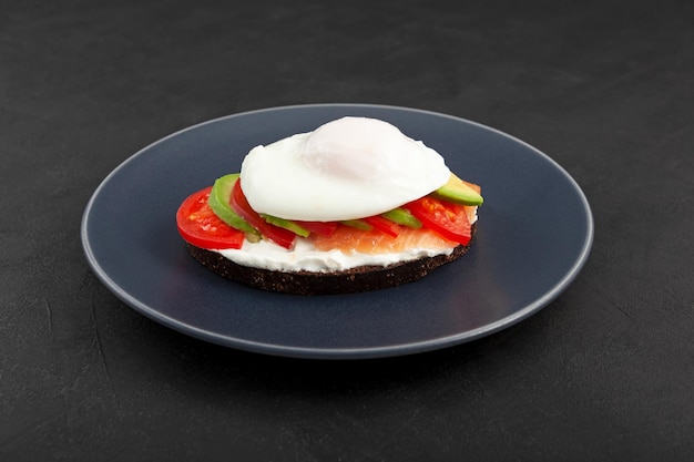 Sandwich or toast with salmon avocado tomatoes and cream cheese on plate closeup